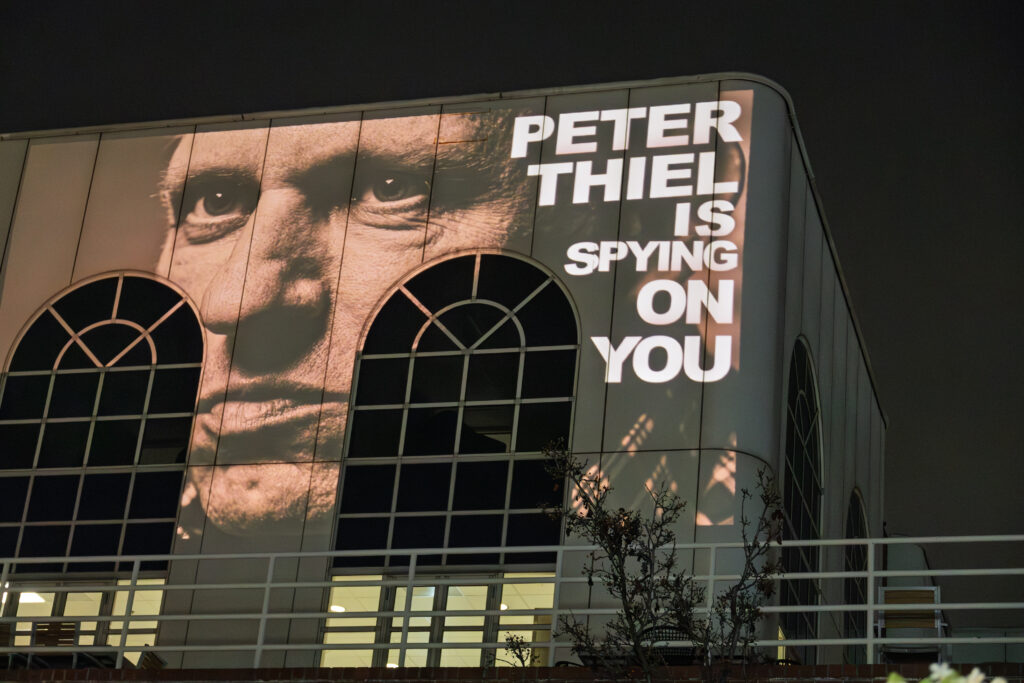 Palantir Technologies was founded in 2003 by Peter Thiel, Alex Karp, Joe Lonsdale, Stephen Cohen, and Nathan Gettings. Photo: Projection Upon Palantir Office by ICE out of Santa Clara County. (ProBonoPhoto.org/Jesse Kornblum). CC-NC-BY-4.0